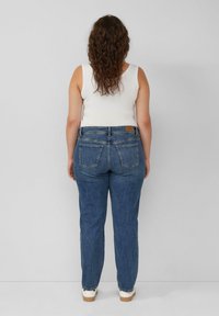 Blauwe spijkerbroek met een rechte pasvorm, voorzien van achterzakken en een leren merklabel op de taille, gestyled met een witte tanktop.