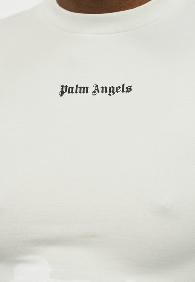 Κοντινό πλάνο λευκού T-shirt με την επιγραφή "Palm Angels" σε μαύρη γοτθική γραμματοσειρά στο στήθος.