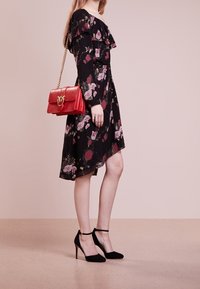 Abito nero a fiori con balze, caratterizzato da fiori rosa e bordeaux. Abbinato a una borsa rossa e a scarpe con tacchi alti in suede neri.
