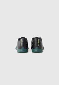 Par de zapatillas deportivas negras y turquesas con la marca "ULTRA" en el talón, mostradas desde la parte trasera sobre un fondo blanco liso.