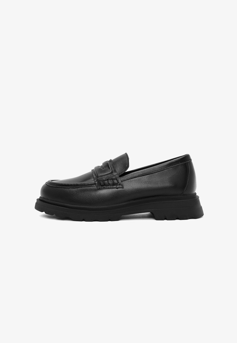 Mocassins en cuir noir avec un devant texturé, un col rembourré et une semelle en caoutchouc épaisse, présentant un design à profil bas et des détails de couture subtils.