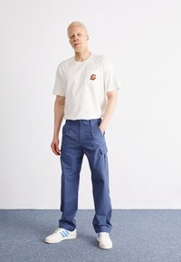 Witte katoenen t-shirt met een borstzak en geborduurd ontwerp, gecombineerd met blauwe cargobroek met zijzakken en een relaxte pasvorm.