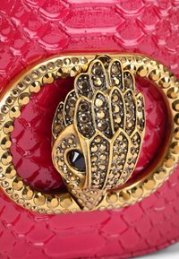Borsa rosa con texture a forma di coccodrillo, dotata di una chiusura dorata con un design di mano dettagliato e decorazioni incastonate. Finitura lucida.