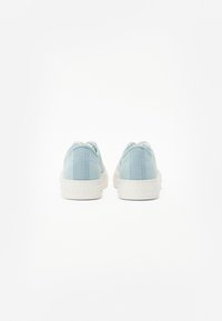 Světlomodré plátěné tenisky s bílými gumovými podrážkami a texturovanými akcenty na zadní části, s minimalistickým designem a zaobleným tvarem špičky.