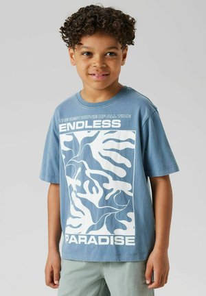 T-shirt bleu à manches courtes avec un motif abstrait blanc et un texte en gras portant "PARADIS SANS FIN" sur le devant.