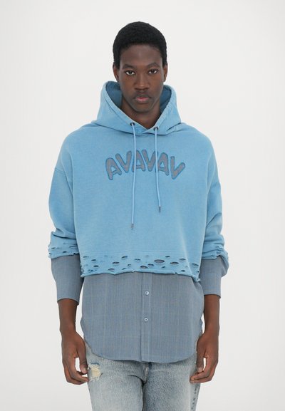 Light blue cropped hoodie with "AVAVAV" embroidery, distressed hem, layered over a blue and white striped long-sleeve shirt, denim jeans.