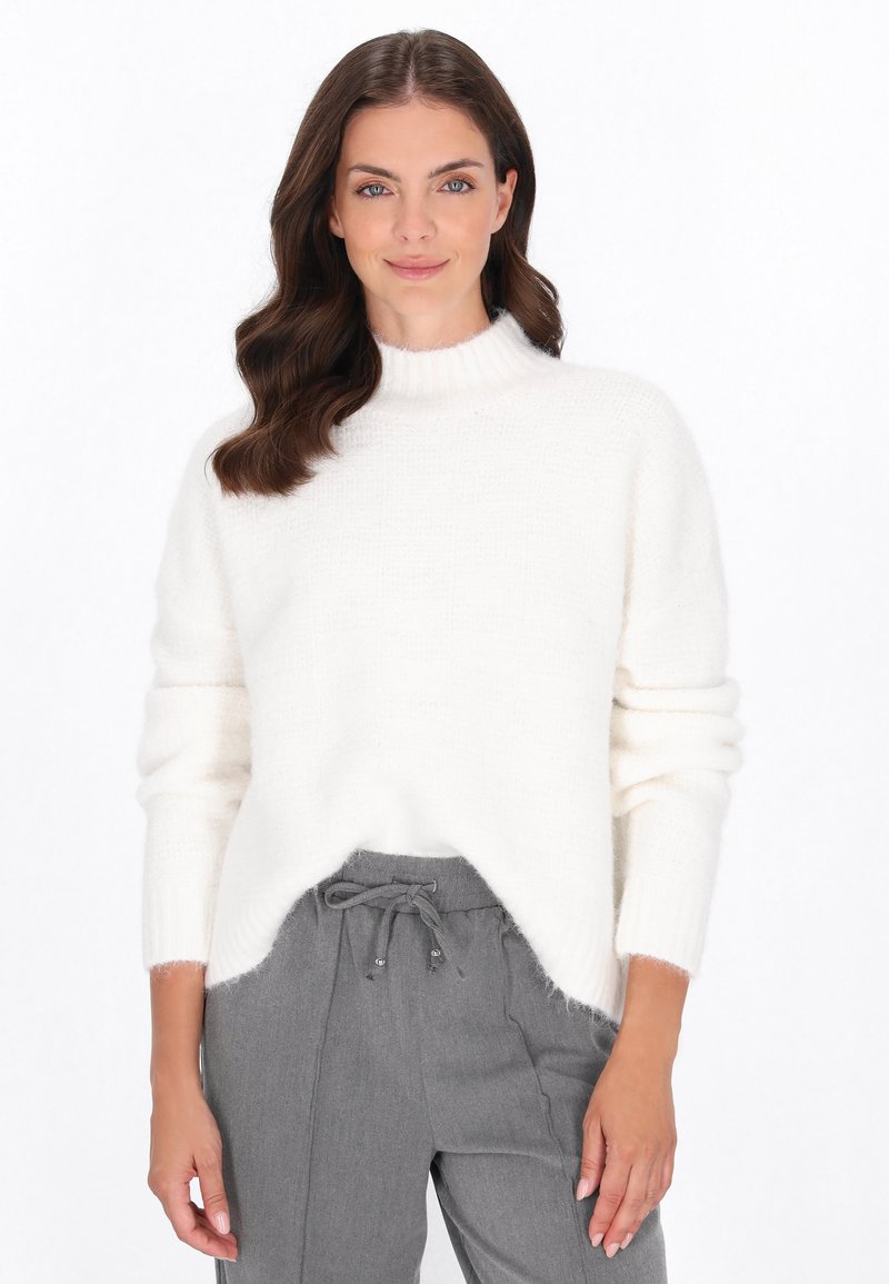 Witte, fluffy gebreide sweater met een hoge ribbels boord, lange mouwen en een licht afgeronde zoom. Gecombineerd met grijze, loszittende broek.