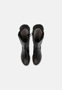 Paire de bottes en cuir noir mi-mollet avec semelles marron, fermetures éclair latérales et doublure intérieure grise, vues de dessus sur un fond blanc.