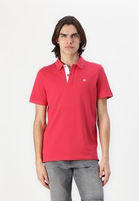 Polo shirt rouge à manches courtes et col, avec une patte de boutonnage blanche et un petit logo sur la poitrine gauche.