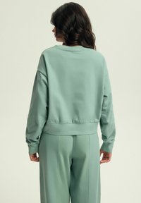 Miętowa bluza z luźnym krojem, ściągaczami przy mankietach i w pasie. Miękka tkanina i prosty design, noszona z pasującymi spodniami.