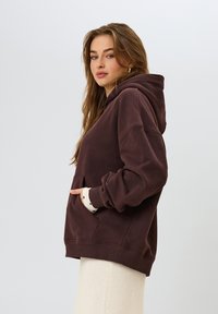 Sudadera oversized marrón hecha de un tejido suave, con un bolsillo frontal, capucha con cordón y puños contrastantes con un patrón de lunares.