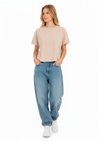 T-shirt corta beige con maniche arrotolate, abbinata a jeans larghi blu chiaro e sneakers bianche; design semplice, texture morbida.