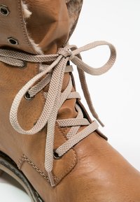 Gros plan d'une botte en cuir marron clair avec des lacets beige noués en nœud et une doublure en fourrure douce visible autour de la cheville.