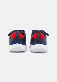Baskets de sport bleu foncé avec des accents rouges et gris, des panneaux en maille, une languette de traction et une semelle en caoutchouc blanc avec un revêtement texturé.