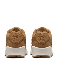 Nike Air tenisice s gornjim dijelom u boji tamne bež, strukturiranim detaljima i bijelom potplatu. Imaju logo na peti i podstavljeni ovratnik za udobnost.
