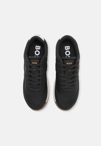 Svarta träningsskor med texturerad syntetisk ovandel, snörning, vadderad plös och kontrasterande vita och bruna sulor.