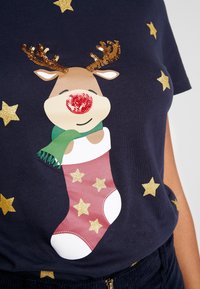 Marinblå t-shirt med kort ärm som har en ren grafik med glittriga horn och en röd näsa, bredvid en rosa julstrumpa och guldstjärnor.