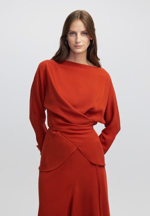 Abito rosso con scollatura drappeggiata, maniche lunghe e orlo asimmetrico a strati. Realizzato in tessuto morbido con un design fluido.
