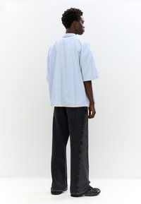 Camicetta a maniche corte a righe in blu chiaro e bianco, abbinata a jeans neri a vestibilità larga, con una silhouette rilassata e tasche laterali.
