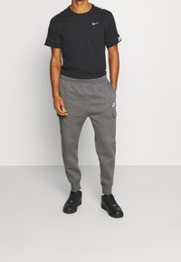 Svart Nike t-shirt med korta ärmar och logotyp, i kombination med gråa sweatpants med fickor och en liten logotyp, buren med svarta sneakers.