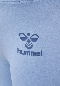 Jasnoniebieskie spodnie sportowe wykonane z elastycznego materiału. Posiadają ciemnoniebieskie logo z motywem pszczoły oraz napisem "hummel" poniżej.