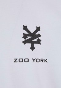 Hvid t-shirt med et sort, stiliseret logo over teksten "ZOO YORK" i fed sort skrift. Blødt bomuldsstof, korte ærmer.