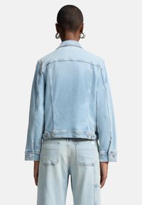 Ljusblå denimjacka med en kortad design, synliga sömnadsdetaljer, standardkrage och knappade ärmslut. Slät textur, klassisk siluett.