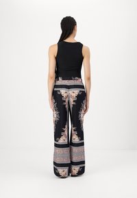 Fekete ujjatlan felső széles lábú nadrággal párosítva, amelynek virágmintája rózsaszín és krém színű egy fekete háttéren, díszes szegélyekkel.