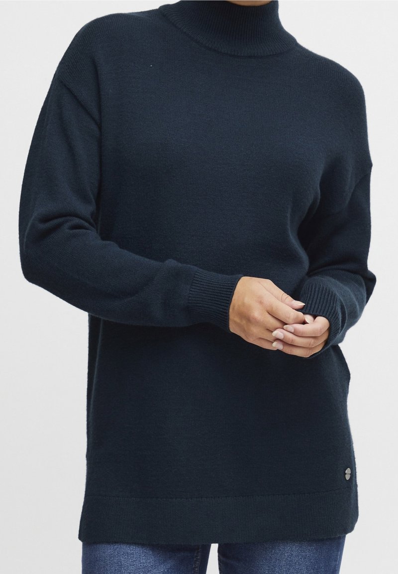 Granatowy, ciemny, dziany sweter z golfem o luźnym kroju, z prążkowanymi mankietami i brzegiem. Zawiera małe logo na dole po lewej stronie.