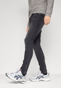 Jeans negros de corte ajustado, con una textura de denim suave. Combinados con zapatillas deportivas blancas y grises con detalles de acento.