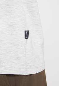 Tricou gri deschis dintr-un amestec moale de bumbac. Prezintă o etichetă mică bleumarin pe care este cusut textul "PIER ONE" pe partea laterală. Textură netedă, croi clasic.