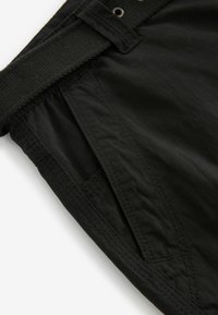 Sorte stofshorts med en tekstureret overflade, der har en bred talje, sidelomme og synlige syninger.