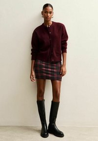 Burgundy wool cardigan with a round neck and buttons, paired with a plaid mini skirt in red and green tones, and knee-high black boots.