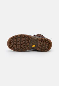 Braune Wanderschuhsohle mit tiefen Profilen, auffälligem gelbem Logo, strukturiertem Gummi für besseren Grip und einem robusten Design, das sich für die Nutzung im Freien eignet.