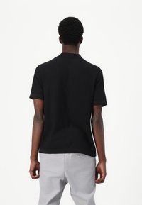 Black short-sleeve polo shirt made of textured fabric, featuring a collared neck and a straight hem, paired with light gray pants.