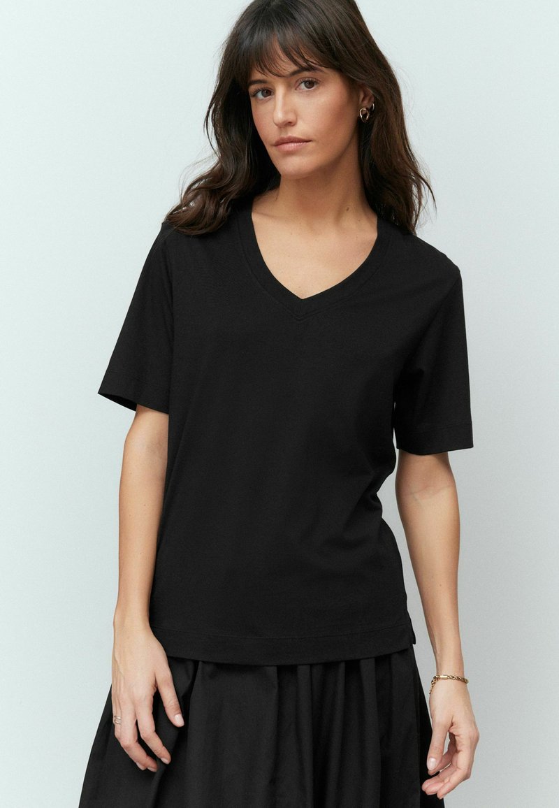 Sort V-hals t-shirt med korte ærmer, lavet af blødt bomuld. Har en afslappet pasform og glat tekstur. Bæres med en sort nederdel.
