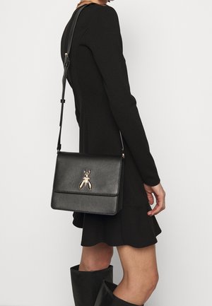 Sac bandoulière en cuir noir avec une finition texturée, orné d'un accent doré en forme d'insecte. Bretelle ajustable, forme rectangulaire, design minimaliste.