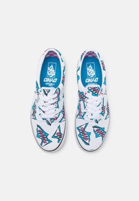 Baskets en toile blanches avec un motif géométrique coloré en bleu et rose. Design à lacets avec une semelle intérieure bleue affichant le logo de la marque.
