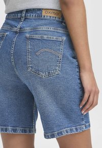 Shorts in denim di colore azzurro chiaro, con cuciture bianche, un'etichetta in pelle sulla vita e una singola tasca posteriore con dettaglio di cucitura ad arco.