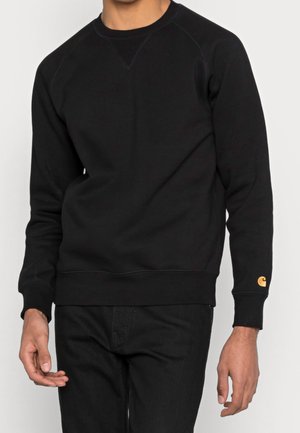 Męskie tułów ubrany w gładką czarną bluzę z długim rękawem, z małym żółtym logo na lewym mankiecie, oraz pasujące czarne spodnie.