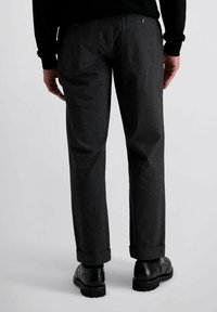 Grijze op maat gemaakte broek van een gestructureerde stof, met een rechte snit en opgerolde cuffs. Achterzakken met knopen, gecombineerd met zwarte schoenen.