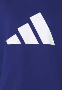 T-shirt in cotone blu con un grande logo bianco a tre strisce sul davanti. La texture appare liscia con un design a vestibilità regolare.