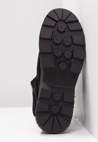 Bota de ante negra con suela de goma. Presenta un patrón de suela con tacos hexagonales para mayor tracción. Diseño sencillo, suela plana y sin marcas visibles.