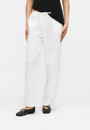 Λευκό φαρδύ παντελόνι με κεντήματα λουλουδιών και ελαστική μέση με κορδόνι, φορεμένο με μαύρο τοπ και μαύρες μπαλαρίνες.