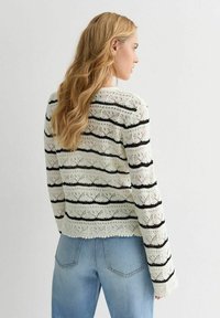 Lace-Strickpullover in Creme mit schwarzen horizontalen Streifen. Verfügt über einen runden Ausschnitt und lange Ärmel, kombiniert mit hellblauen Jeans.