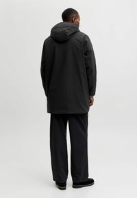 Czarna wodoodporna kurtka z kapturem, o prostym kroju i długich rękawach, w połączeniu z luźnymi czarnymi spodniami i ciemnym obuwiem.