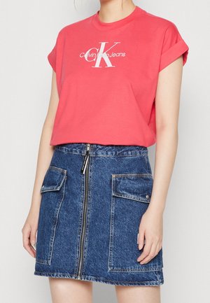 Persona con una camiseta roja de Calvin Klein Jeans con las mangas remangadas y una falda vaquera azul con cremallera frontal y bolsillos con solapa.