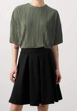 Top verde plissettato con maniche corte, abbinato a una gonna nera a pieghe al ginocchio. Materiale in misto cotone. Design semplice e strutturato.