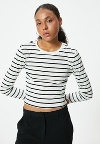 Korte mouw cropped top in het wit met zwarte horizontale strepen. Beschikt over een ronde halslijn en een getailleerd ontwerp. Gekocht met hoge taille zwarte broeken.