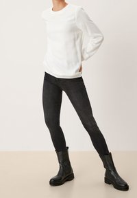 Top blanco de manga larga con cuello redondo, combinado con jeans skinny negros y botas negras hasta el tobillo, con una textura suave y un diseño ajustado.